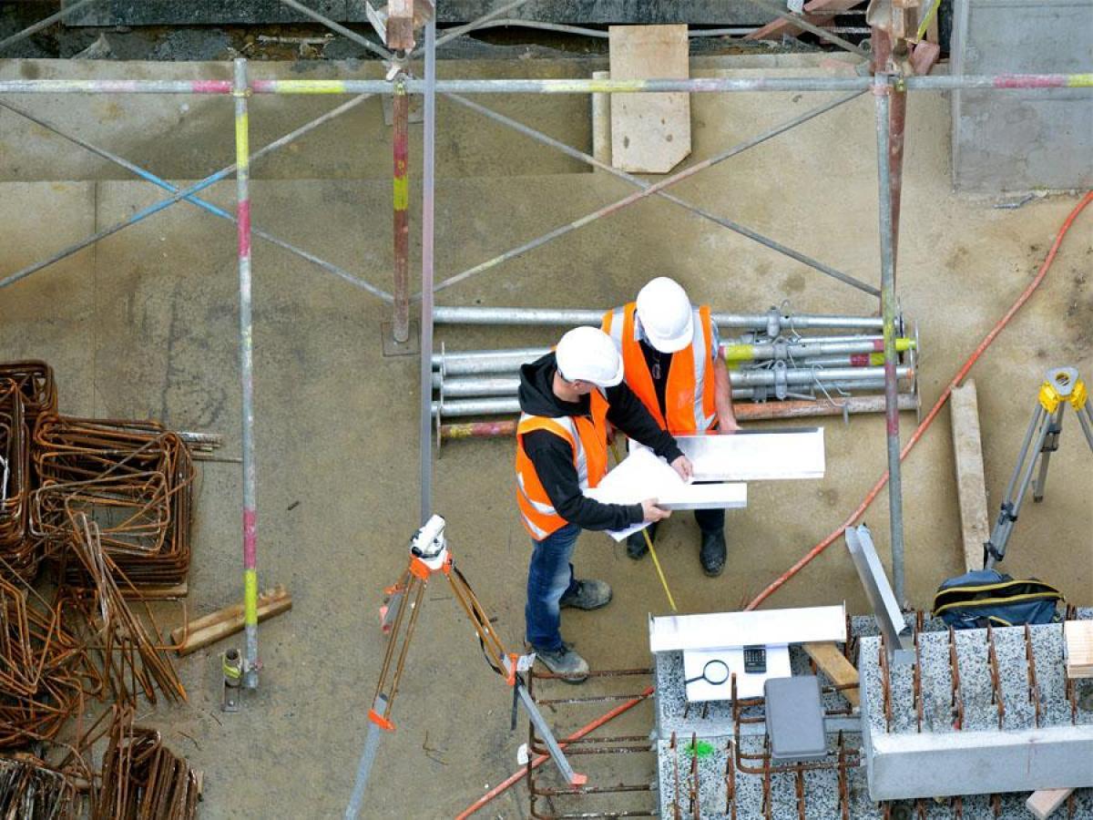 Two engineers on a worksite, wearing personal protective equipment, looking at paperwork