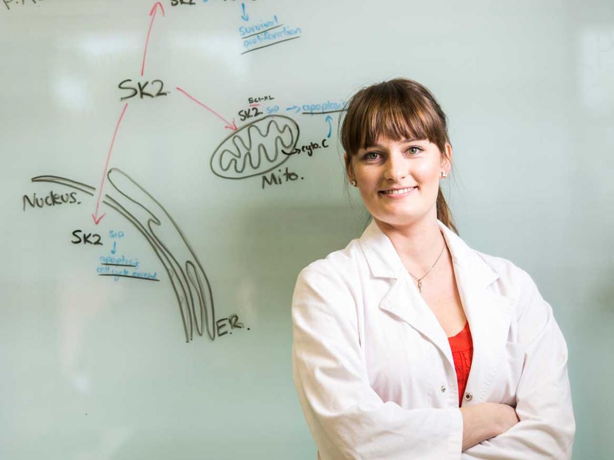 Student in lab coat in front of white board