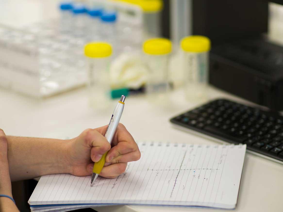 A hand writing notes in a lab / practical classroom