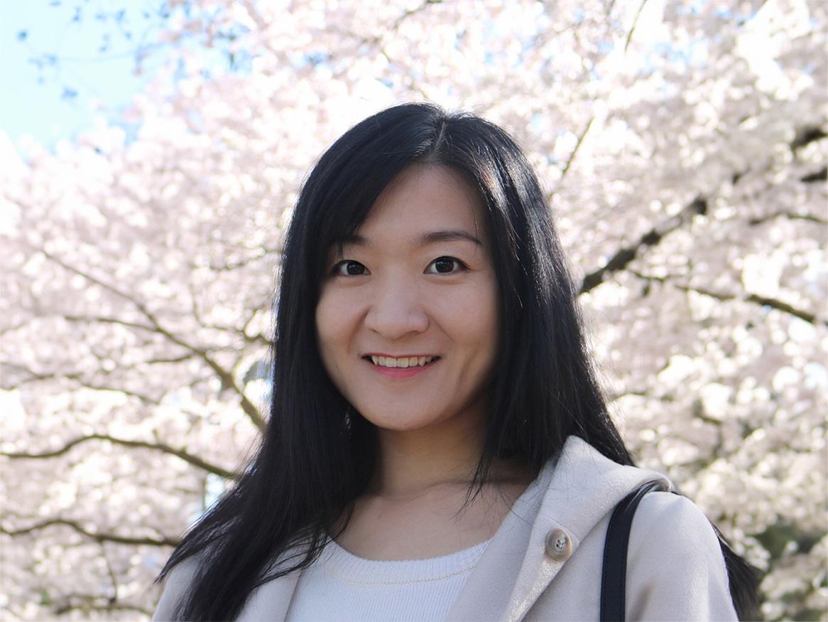 Yujie Chen smiling with cherry blossoms in the background