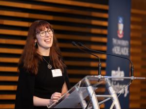 woman speaking at a lecturn with long brown hair and glasses