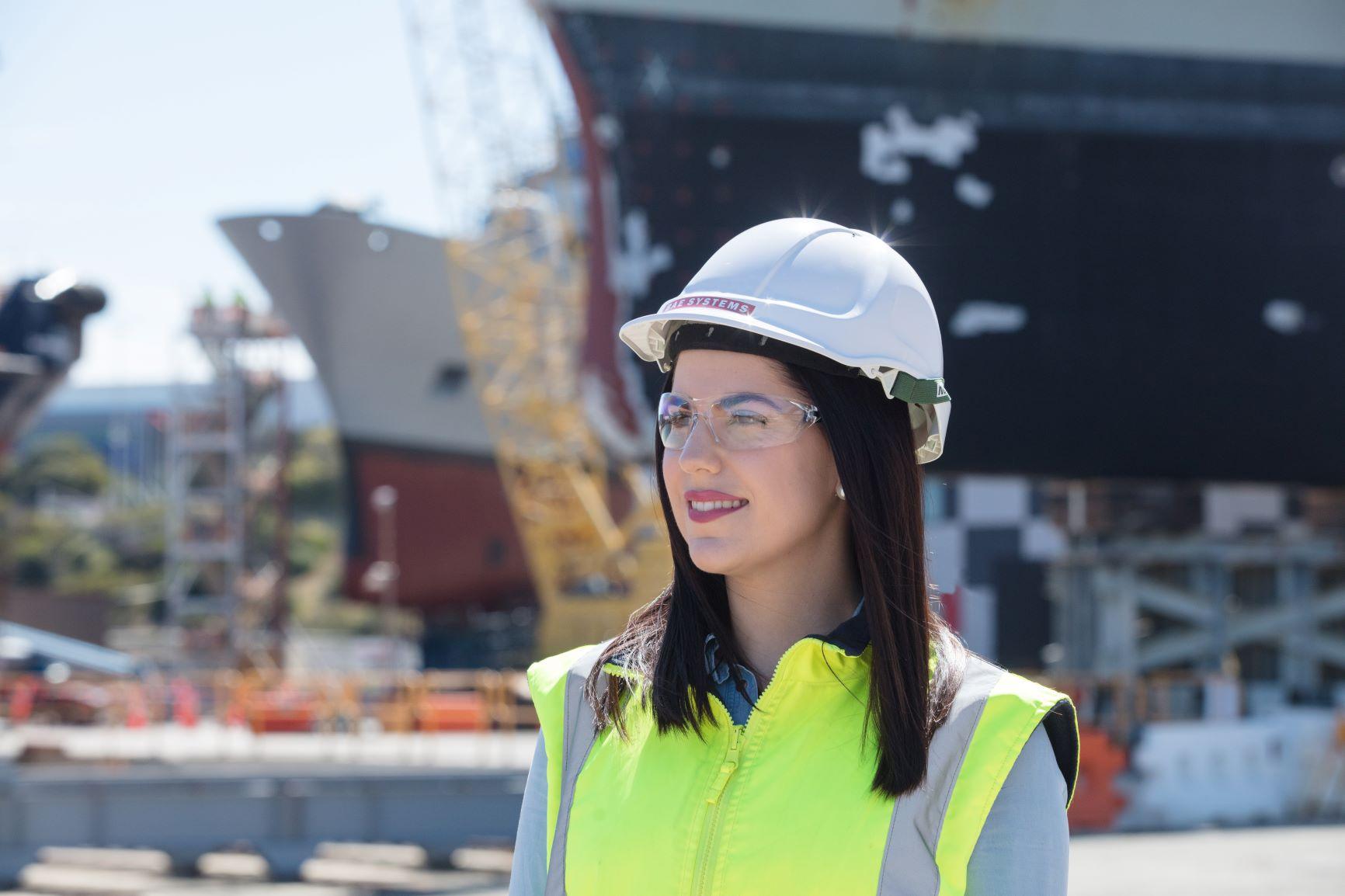 BAE Graduate program, female student wearing a hardhat in front of a ship