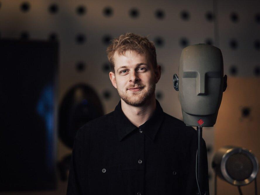 Hacker Exchange: student standing against a dark background with a robot face in front of him