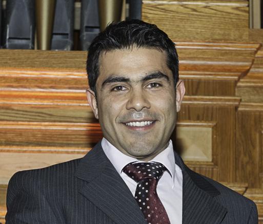 Abbas Zeinijahromi wearing a suit and tie, smiling in front of a wooden background
