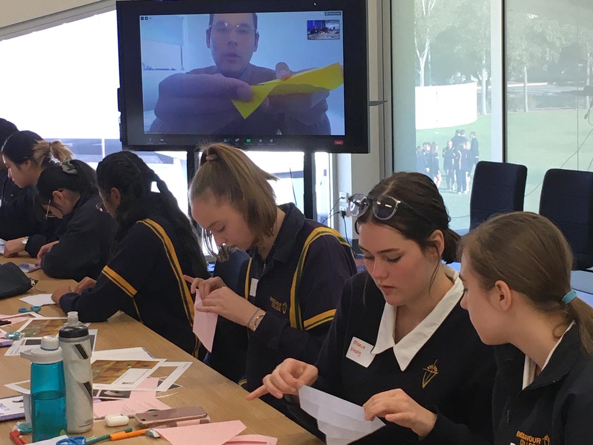 A class of female high school students working on a construction project with a tv screen in the background livestreaming the instructor