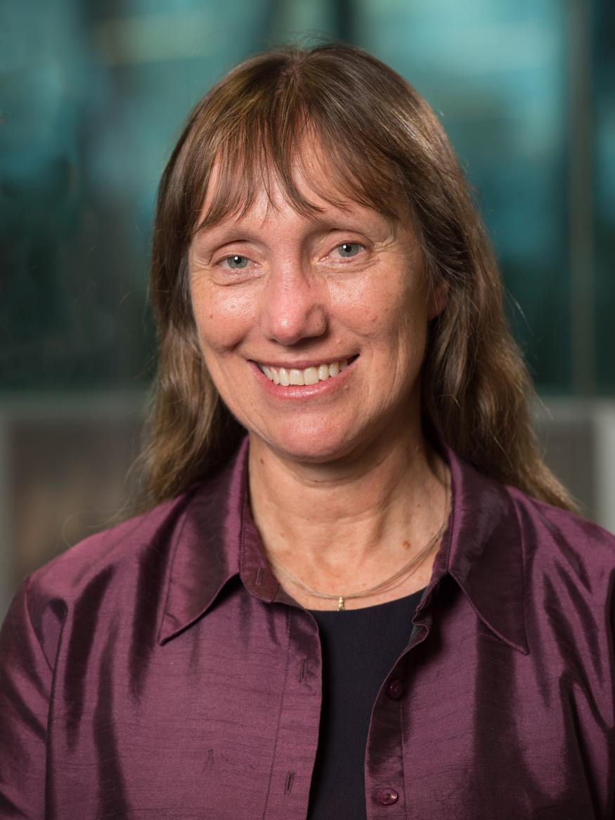 Image of a woman smiling with brown hair and a fringe, wearing a shiny purple shirt.