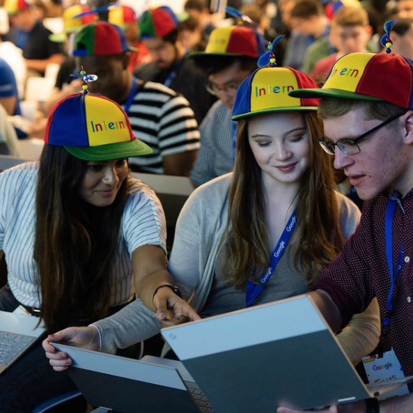 Google interns sitting in a hall with propeller caps on which say "interns"