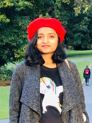 Kavita standing in the Botanic gardens wearing a bright red hat.