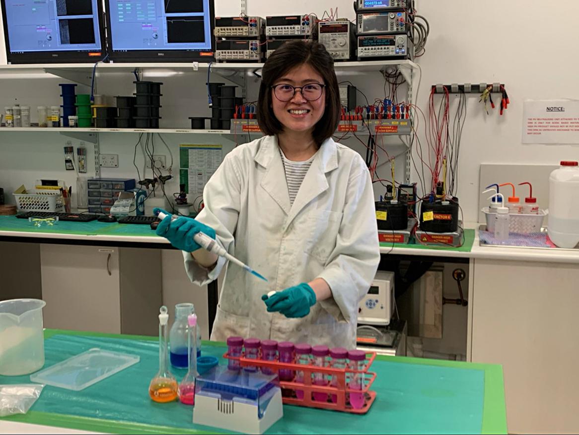 Dr Cheryl Suwen Law stands smiling in a lab wearing a lab coat