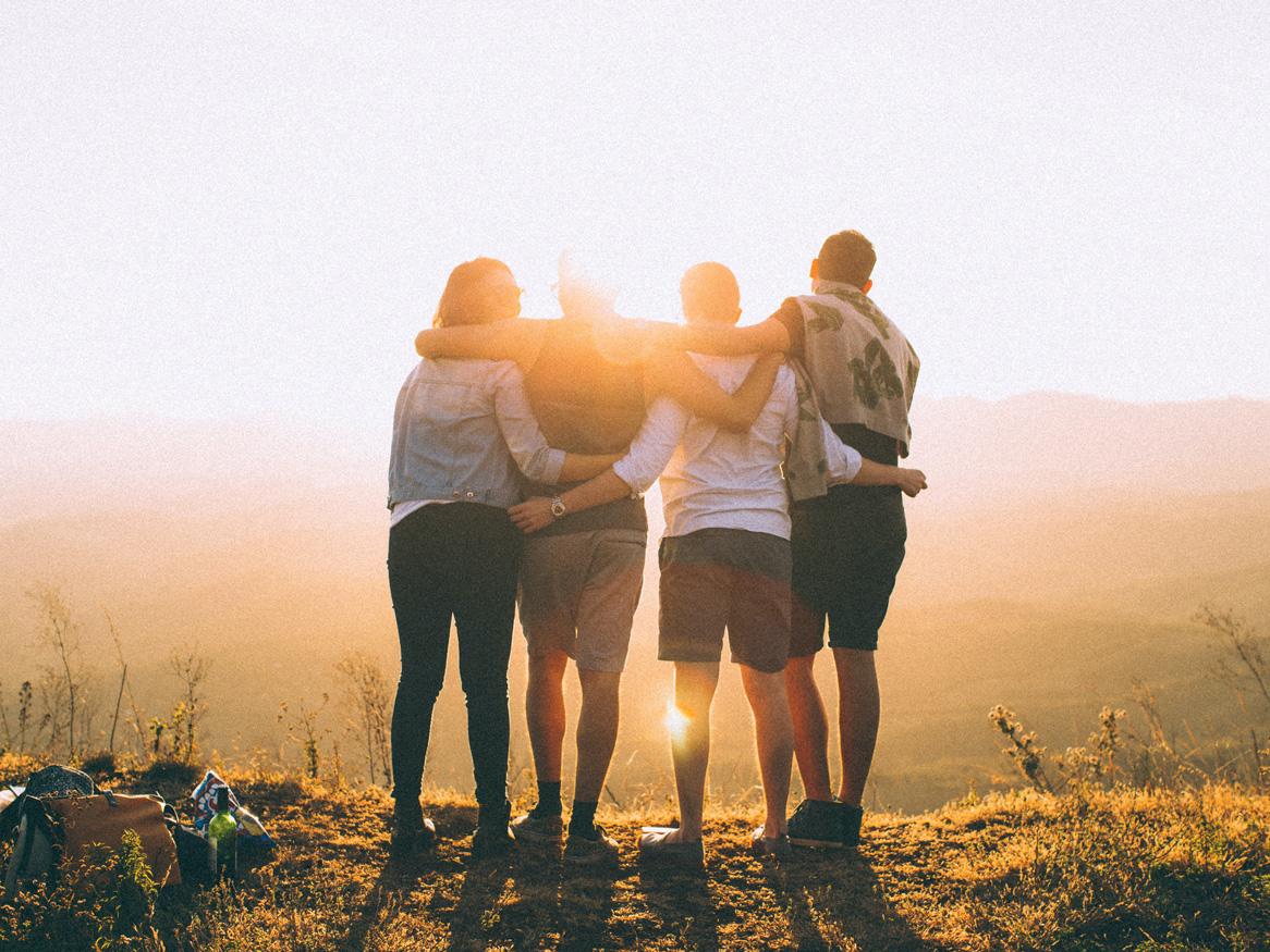 Group of four friends standing arm in arm, obscured by the sunset