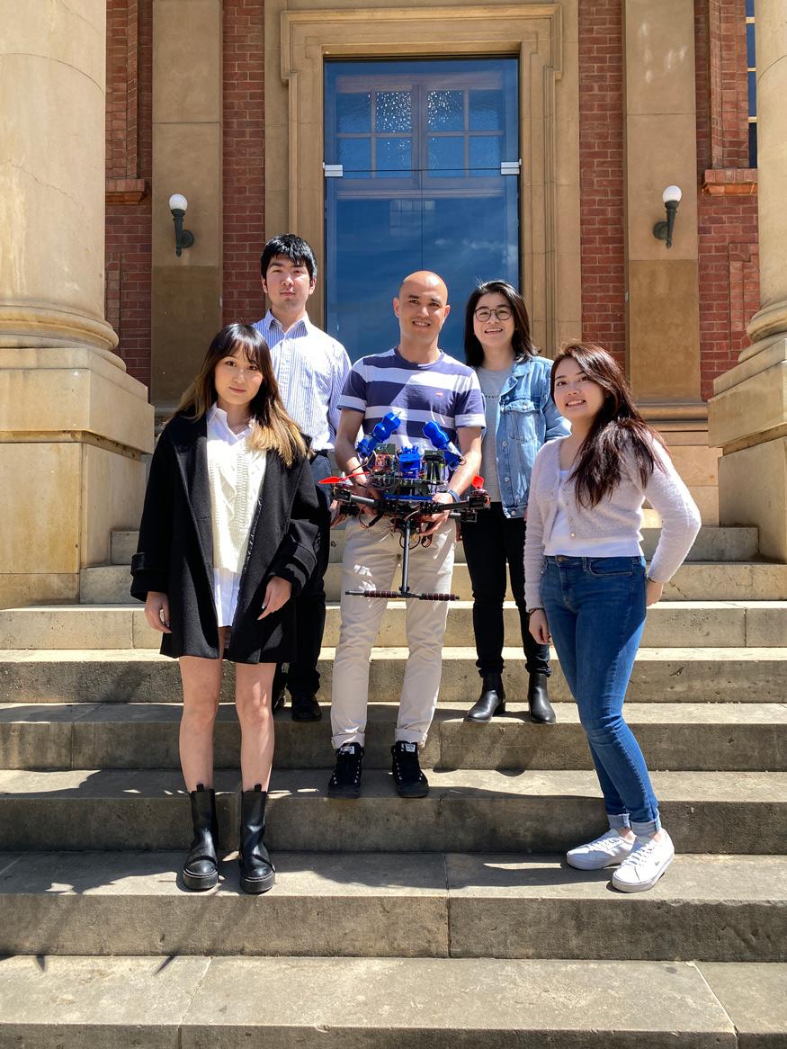 photo of five students holding a robot on some steps