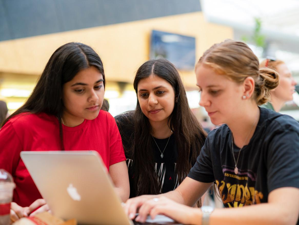 group of three women around a laptop outside