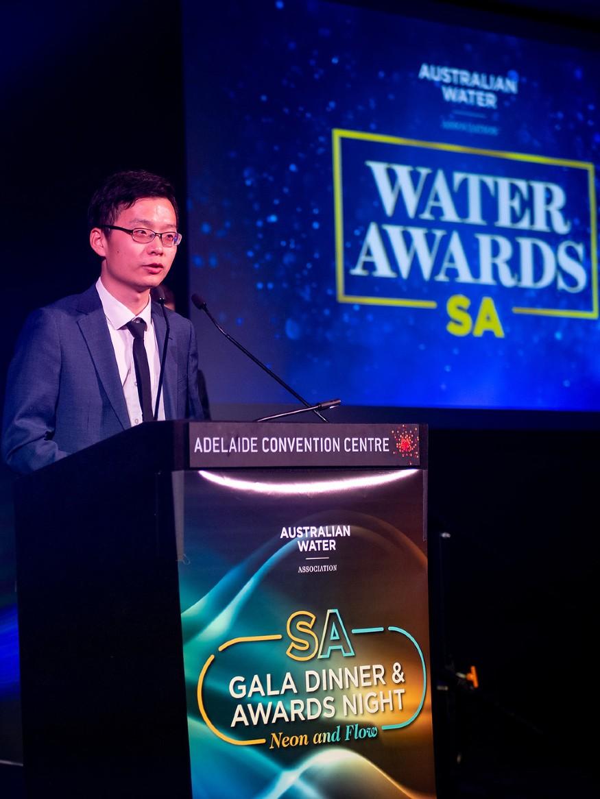 Wei Zing in suit, tie and glasses at podium