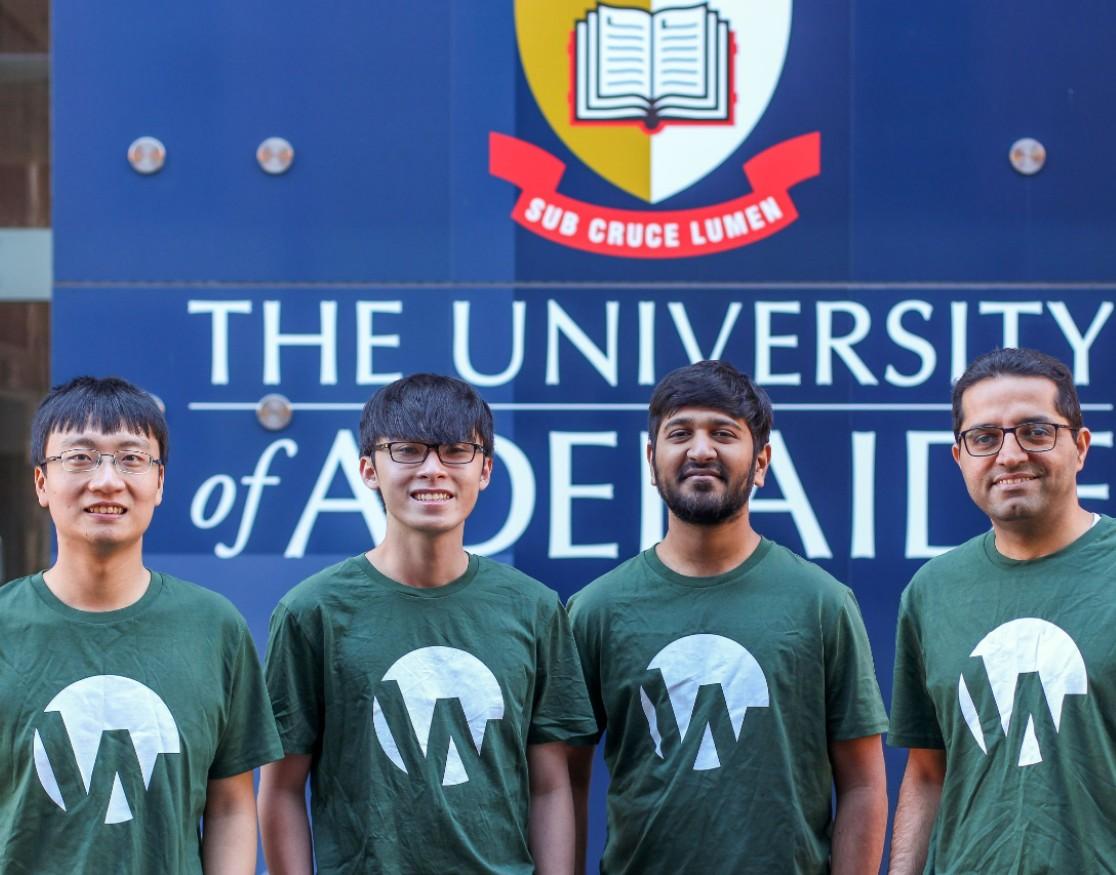 Four men in green t-shirts in front of Uni of Adelaide sign