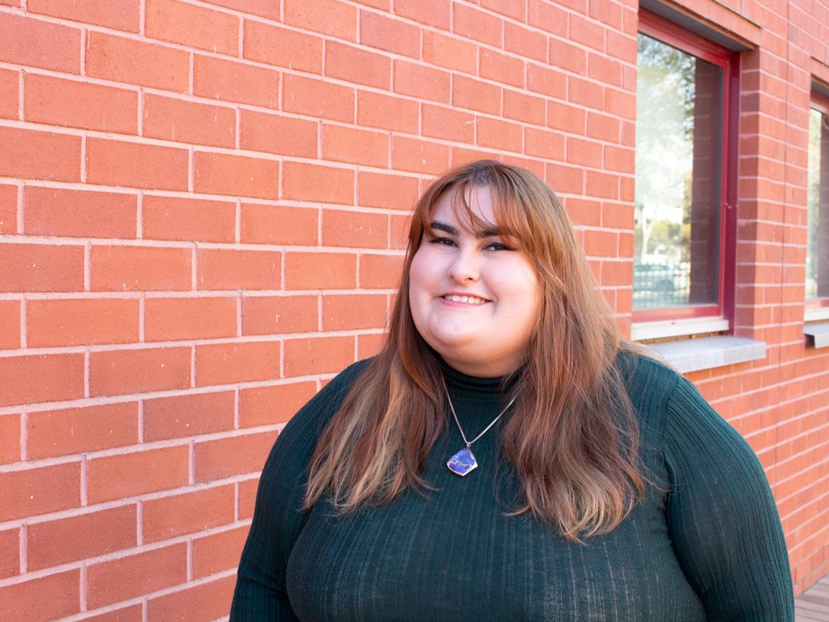 image of a woman with brown hair wearing a green top in front of a red wall