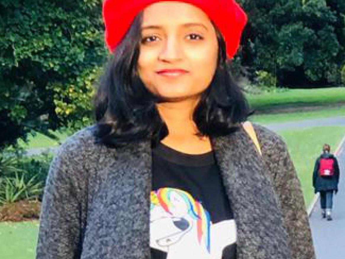Kavita standing in the Botanic gardens wearing a bright red hat.