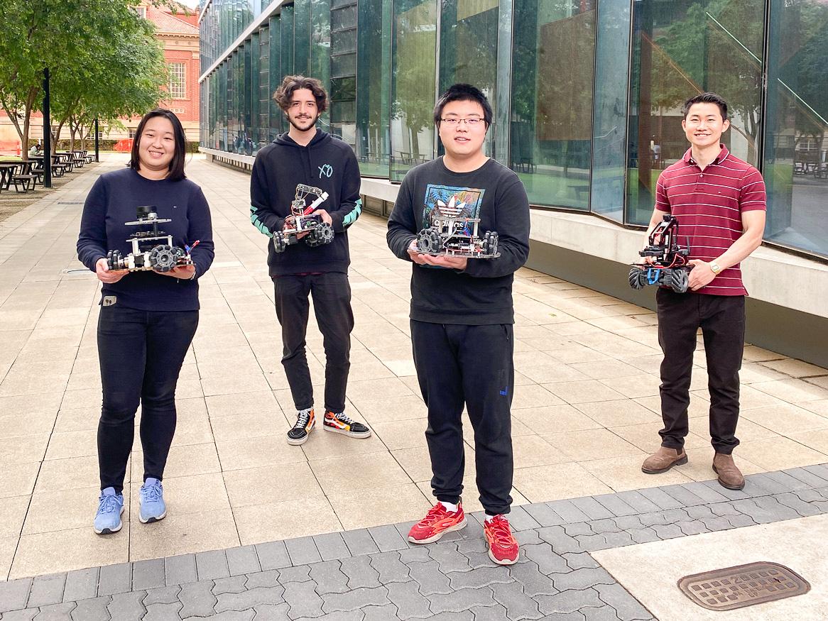 four people standing outside holding robots