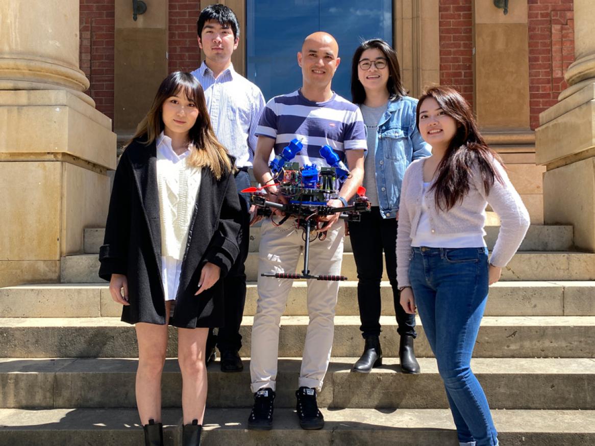 photo of five students holding a robot on some steps