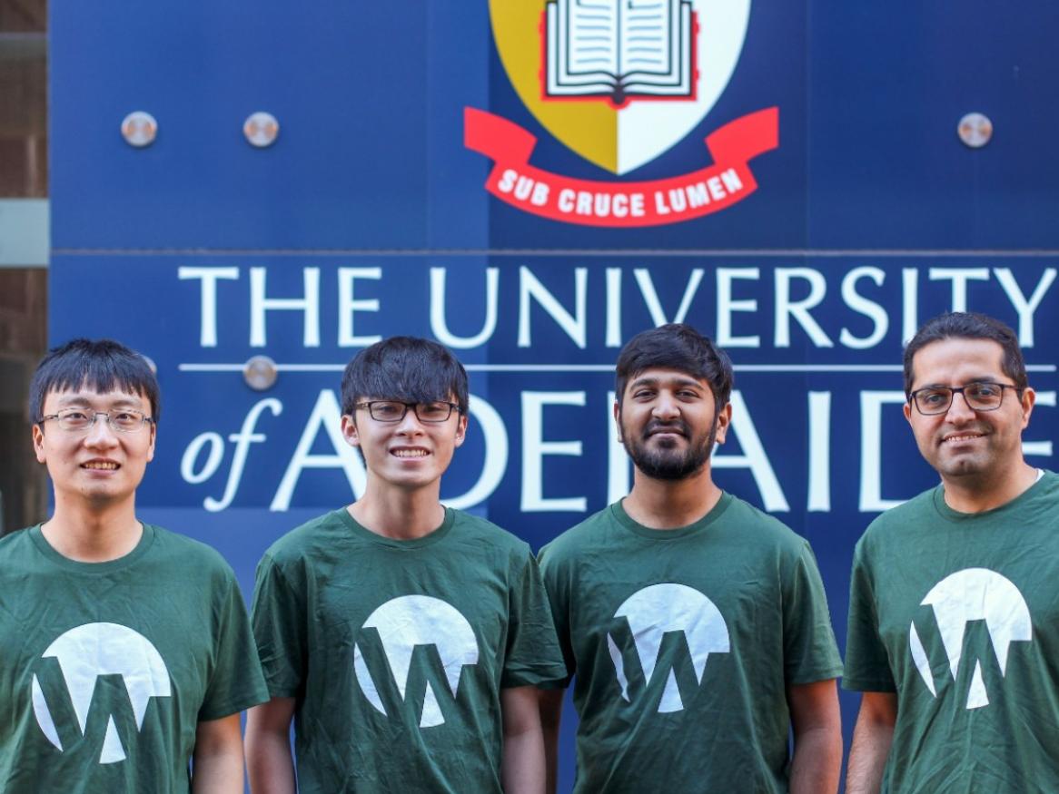 Four men in green t-shirts in front of Uni of Adelaide sign